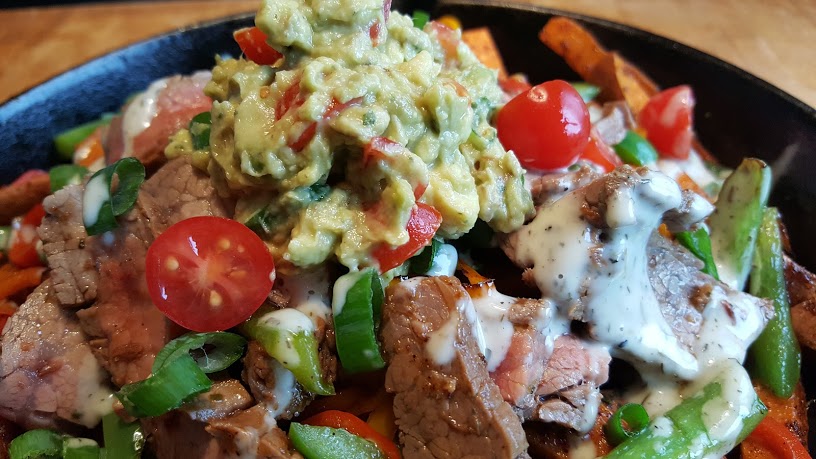 Whole30 Loaded Sweet Potato Fries topped with guacamole green onion and tomatoes.